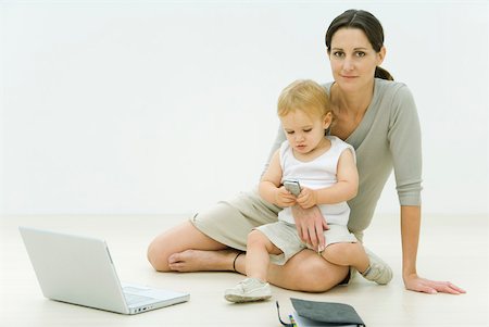single mom - Professional woman sitting on the ground with laptop, holding toddler on lap, toddler looking at cell phone Stock Photo - Premium Royalty-Free, Code: 632-02227967