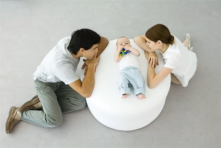 simsearch:632-03027302,k - Young parents leaning against ottoman, looking at baby lying between them Stock Photo - Premium Royalty-Free, Code: 632-02282487
