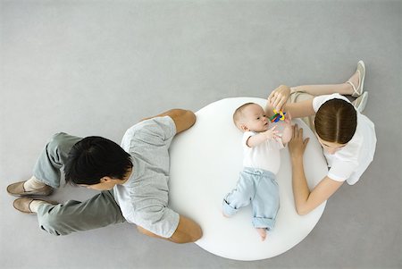 simsearch:632-03027302,k - Mother playing with infant lying on ottoman, father sitting with back turned to them, overhead view Stock Photo - Premium Royalty-Free, Code: 632-02282501