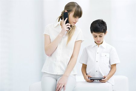 simsearch:632-03424261,k - Woman using cell phone, watching boy play handheld video game Stock Photo - Premium Royalty-Free, Code: 632-02282959