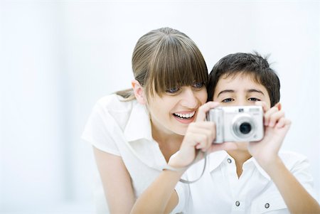 Boy taking picture with camera, mother leaning over his shoulder, smiling Stock Photo - Premium Royalty-Free, Code: 632-02282996