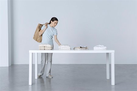 Woman looking at clothing folded on table, shopping bags slung over her shoulder Stock Photo - Premium Royalty-Free, Code: 632-02283052