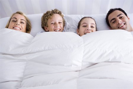 simsearch:632-03424261,k - Family lying together in bed beneath comforter, smiling at camera Stock Photo - Premium Royalty-Free, Code: 632-02345189