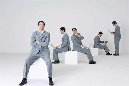 Businessman smiling at camera with arms folded while his clones use laptops in background Foto de stock - Sin royalties Premium, Código: 632-02345572