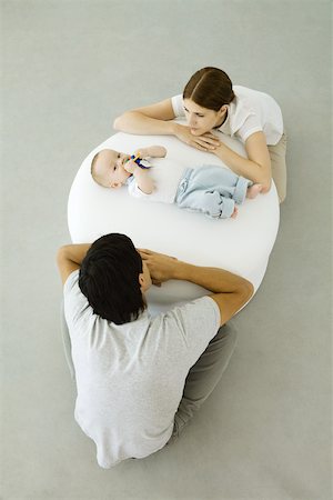 simsearch:632-03027302,k - Young parents leaning against ottoman, looking at baby lying between them Stock Photo - Premium Royalty-Free, Code: 632-02416259