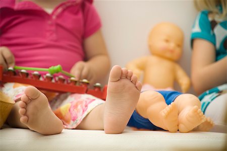 Little girl sitting beside baby doll, close-up of bare feet Stock Photo - Premium Royalty-Free, Code: 632-02645181