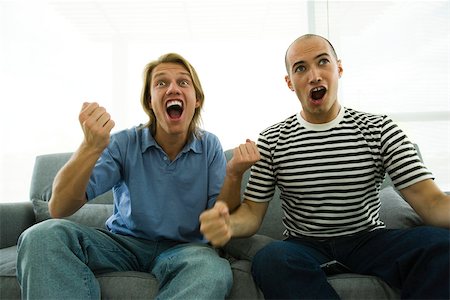 simsearch:628-05817772,k - Two men sitting on sofa watching TV, cheering with clenched fists Stock Photo - Premium Royalty-Free, Code: 632-02744858