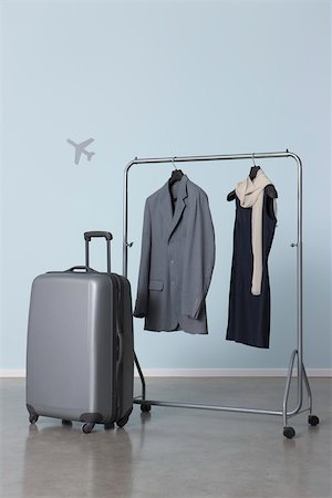 Man's and woman's outfits hanging on clothes rack near suitcase, plane symbol in background Stock Photo - Premium Royalty-Free, Code: 632-02745289