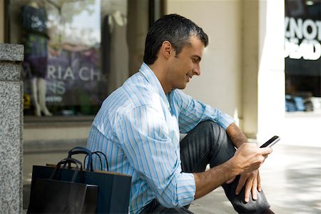 shopfront - Man sitting with outdoors with shopping bags, using cell phone Stock Photo - Premium Royalty-Free, Code: 632-03027439