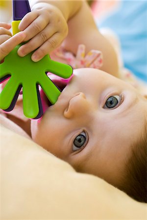 Infant girl chewing on plastic toy, looking at camera Stock Photo - Premium Royalty-Free, Code: 632-03083610