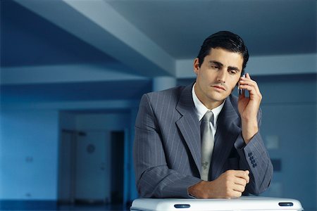 Businessman sitting with briefcase on lap in empty office using cell phone Stock Photo - Premium Royalty-Free, Code: 632-03083704