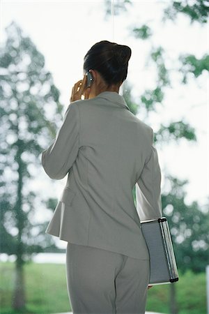 Businesswoman using cell phone, carrying briefcase under arm, rear view Stock Photo - Premium Royalty-Free, Code: 632-03083724