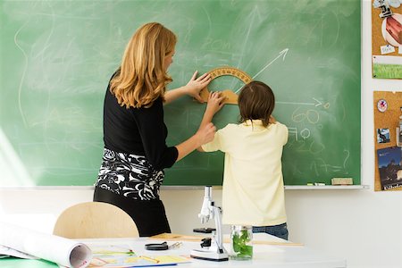 Teacher helping boy draw angle on blackboard using protractor, rear view Stock Photo - Premium Royalty-Free, Code: 632-03193651