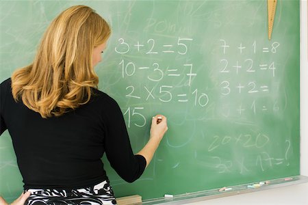 Elementary teacher writing arithmetic on blackboard, rear view Stock Photo - Premium Royalty-Free, Code: 632-03193669
