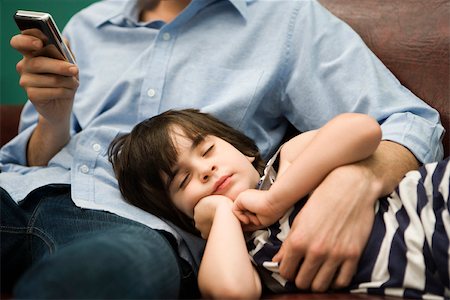 Father text messaging while son naps with head in his lap Stock Photo - Premium Royalty-Free, Code: 632-03424661