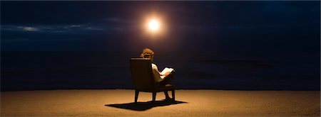 Man sitting in chair under light bulb on beach at night, reading book Stock Photo - Premium Royalty-Free, Code: 632-03500622