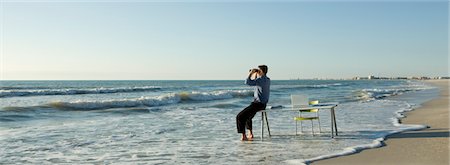 daydreamer (male) - Businessman sitting on desk at the beach, looking through binoculars at sea Stock Photo - Premium Royalty-Free, Code: 632-03500752