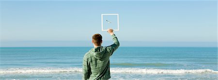 space flight - Man on beach holding up picture frame capturing image of gull flying against blue sky Stock Photo - Premium Royalty-Free, Code: 632-03500761