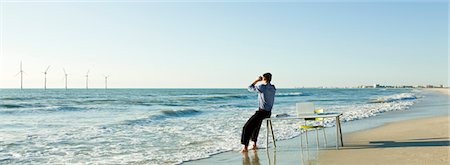 simsearch:632-03500607,k - Man sitting on edge of desk at water's edge on beach looking at offshore wind turbines on horizon Stock Photo - Premium Royalty-Free, Code: 632-03500778