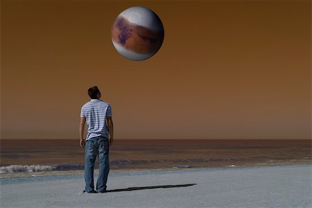simsearch:632-03500607,k - Man on beach looking up at alien world orbiting overhead against brown sky Stock Photo - Premium Royalty-Free, Code: 632-03500788