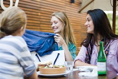Friends having lunch together in outdoor cafe, one woman showing new clothing in shopping bag Stock Photo - Premium Royalty-Free, Code: 632-03516655