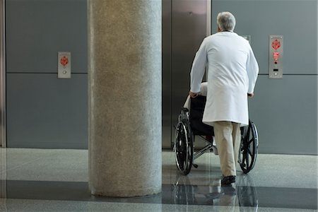 simsearch:632-01613036,k - Doctor pushing patient in wheelchair toward elevator Stock Photo - Premium Royalty-Free, Code: 632-03754346