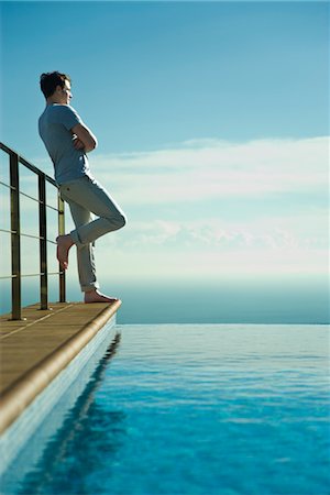 Man leaning against railing beside infinity pool, looking at view Stock Photo - Premium Royalty-Free, Code: 632-03779606