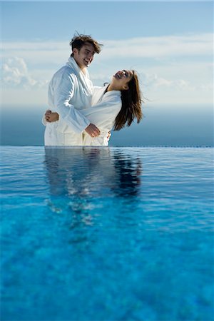 Couple embracing and laughing at edge of infinity pool, both wearing bathrobes Stock Photo - Premium Royalty-Free, Code: 632-03779601