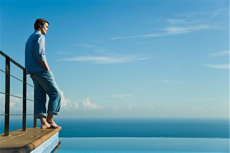 Man standing at edge of infinity pool, looking at view Stock Photo - Premium Royalty-Free, Code: 632-03779612