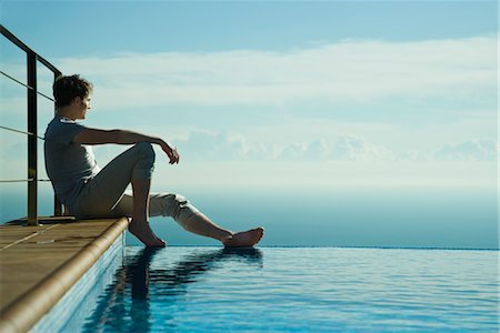 relaxing pool water - Man sitting on edge of infinity pool, looking at view Stock Photo - Premium Royalty-Free, Code: 632-03779622