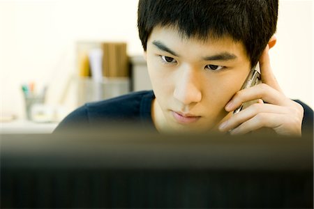 Young man looking at computer monitor and talking on cell phone Stock Photo - Premium Royalty-Free, Code: 632-03898372