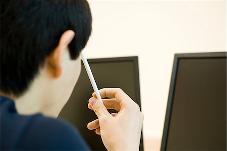 Young man looking at computer monitors, holding pencil against head in thought Stock Photo - Premium Royalty-Free, Code: 632-03898381