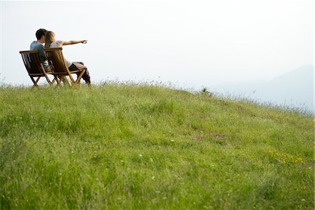 Couple sitting on chairs on top of hill looking at view, woman pointing toward distance Foto de stock - Sin royalties Premium, Código: 633-05401988