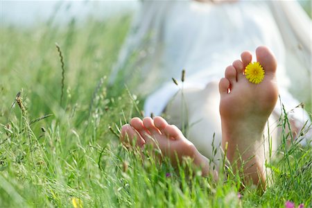Barefoot woman sitting in grass, holding dandelion flower between toes Stock Photo - Premium Royalty-Free, Code: 633-05402096
