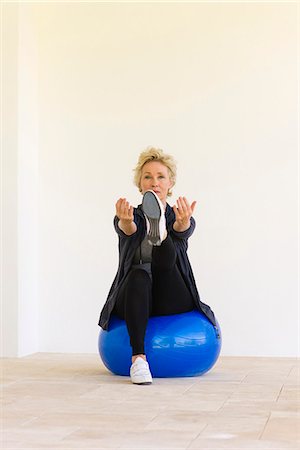 Mature woman sitting on fitness ball with arms out and one leg up Stock Photo - Premium Royalty-Free, Code: 633-06322360