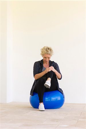 Mature woman sitting on fitness ball, hugging one knee Stock Photo - Premium Royalty-Free, Code: 633-06322531
