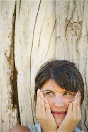 simsearch:632-05760692,k - Woman leaning against tree trunk, smiling and holding face in hands, portrait Stock Photo - Premium Royalty-Free, Code: 633-08150981