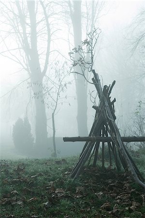 Misty landscape with teepee-shaped log structure in foreground Stock Photo - Premium Royalty-Free, Code: 633-01573345