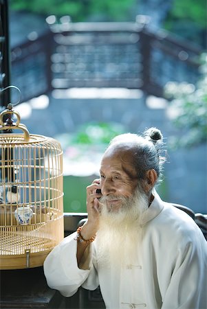 phone one person adult smile elderly - Elderly man wearing traditional Chinese clothing, using cell phone, next to bird cage Stock Photo - Premium Royalty-Free, Code: 633-01714714