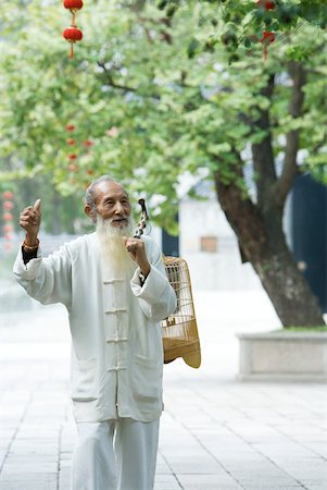 elderly sign - Elderly man wearing traditional Chinese clothing carrying bird cage over shoulder, holding up thumb Stock Photo - Premium Royalty-Free, Code: 633-01714730