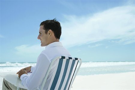 Man sitting in folding chair on beach, using pen and paper, side view Stock Photo - Premium Royalty-Free, Code: 633-01713848