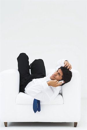 simsearch:632-03403433,k - Businessman lying backwards in armchair, holding cell phone to ear and scratching head, full length Stock Photo - Premium Royalty-Free, Code: 633-01837164