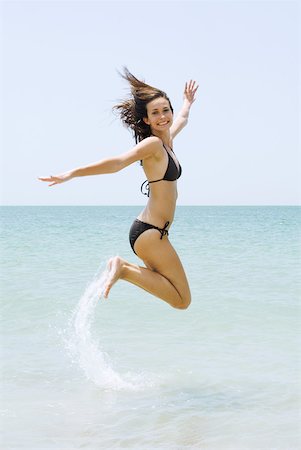 simsearch:633-01714467,k - Young woman in bikini at the beach, jumping in the air, smiling at camera Stock Photo - Premium Royalty-Free, Code: 633-01837184