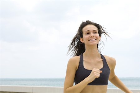 simsearch:633-01715682,k - Young woman in sports bra running outdoors, smiling, looking away Stock Photo - Premium Royalty-Free, Code: 633-01837188