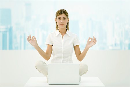 Woman sitting in lotus position on desk with laZSop computer, looking at camera Stock Photo - Premium Royalty-Free, Code: 633-02231726