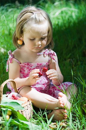 Little girl sitting on the ground holding cherries Stock Photo - Premium Royalty-Free, Code: 633-02417992
