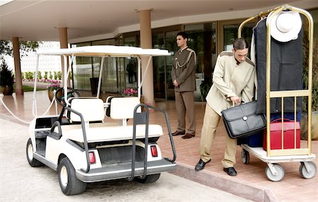 Bellboy delivering luggage to hotel with doorman standing by Stock Photo - Premium Royalty-Free, Code: 644-01435909