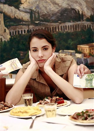 Woman sulking at restaurant table with Euro bills Stock Photo - Premium Royalty-Free, Code: 644-01631416