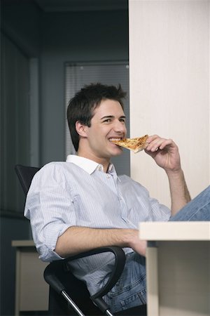 Office worker eating a pizza slice at desk Stock Photo - Premium Royalty-Free, Code: 644-01825238