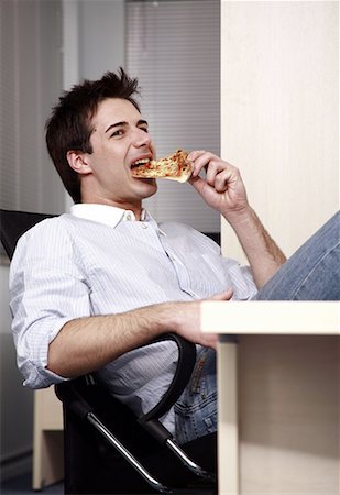 Office worker eating a pizza slice at desk Stock Photo - Premium Royalty-Free, Code: 644-01825277